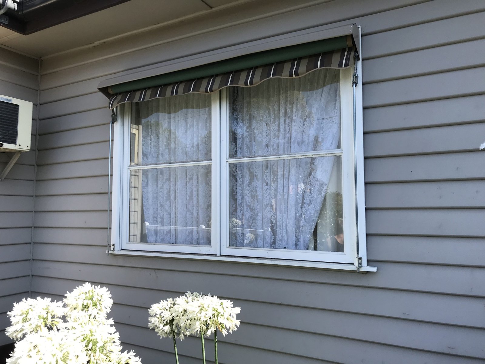 Double-hung white window with lace curtains and green awning